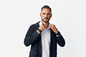 A professional businessman stands against a solid colored backdrop, adjusting his shirt collar with a calm, confident gaze, conveying readiness and determination.