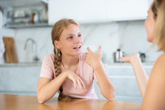 Smiling teenage girl engrossed in lively friendly conversation with woman at home kitchen. Concept of close and trusting relationships between daughter and mother - Powered by Adobe