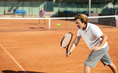 Adult man in sportswear with a tennis racket in his hands plays tennis in the city court