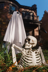 A lifelike skeleton prop rests in the grass beside a white ghost sheet, creating a spooky Halloween scene suitable for outdoor decor, horror, or fall-themed shoots.