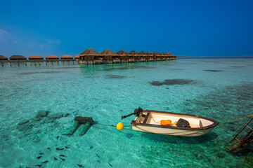 Tranquil closeup calm sea water waves with palm trees. Boat and bungalows background. Tropical island beach landscape exotic shore coast. Summer vacation, holiday amazing nature, Maldives.