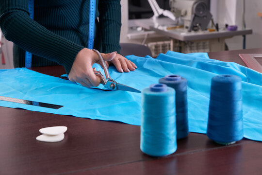 Dressmaker cutting blue fabric in tailor studio, atelier shop