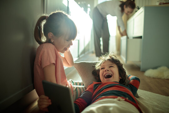 Young children laughing with tablet at home - Powered by Adobe