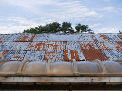 Weathered corrugated metal roofing with rust patches and peeling paint against blue sky