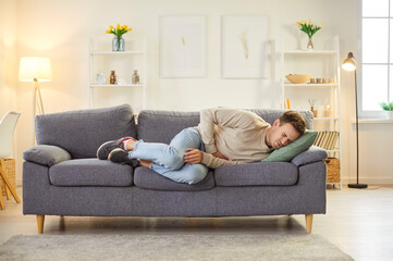 Young man feeling unwell, suffering from stomach ache or digestive disorder, lying on sofa in...