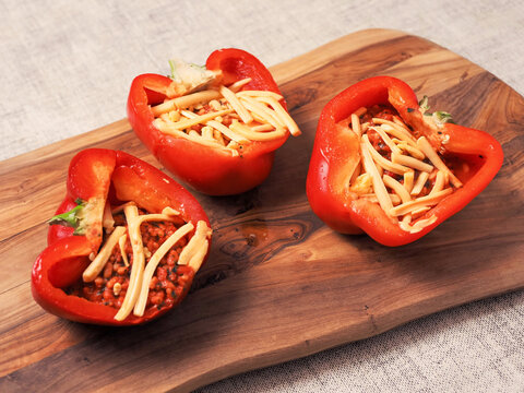 Fine red stuffed red peppers with rice, herbs and cheese on wooden cutting board. Premium high quality food with tasty ingredients. Cooking fancy dish. - Powered by Adobe