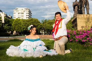 A hispanic couple sits on green grass in traditional dress and looking at the camera in downtown Neiva, Huila, Colombia. Concept of Colombian culture