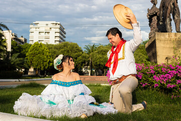 A couple of Latinos dancers sit on green grass in traditional dress in downtown Neiva, Huila, Colombia. Concept of Colombian culture