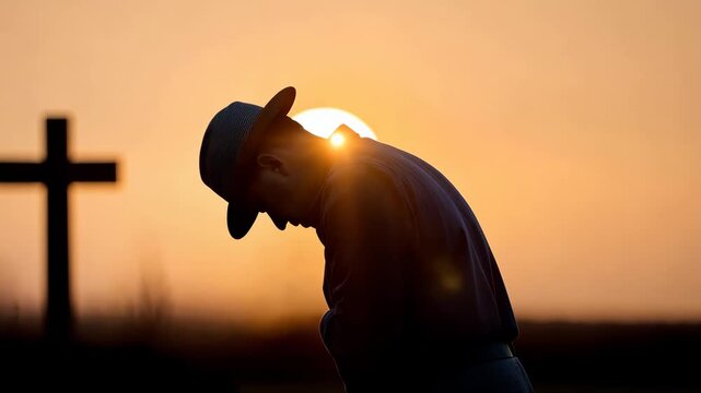 Reflective silhouette at sunset with cross: male in prayerful pose