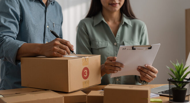 young couple working on small business orders in home office with cardboard boxes and clipboard