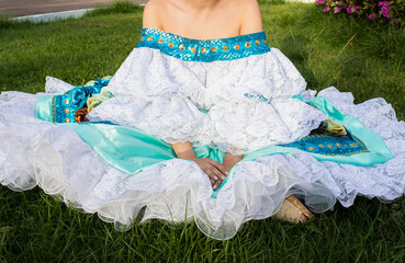 Portrait of an unrecognizable Colombian dancer in a traditional dress sitting on grass in Neiva, Huila, Colombia. Concept of Colombian culture