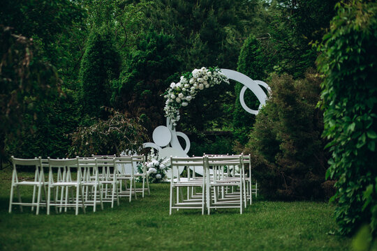Outdoor wedding ceremony setup with white chairs and floral arch in lush garden