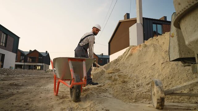Construction worker shoveling sand into wheelbarrow
