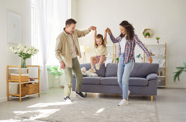 Family parents support daughter play at home. In livingroom, the child girl laughs with mother and...