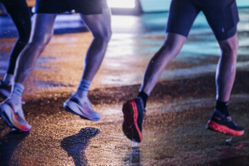 Night marathon runners crowd in the rain, sportsmen participants start running the half-marathon in the city streets with night lighting and illumination, group crowd of sportswomen joggers in motion
