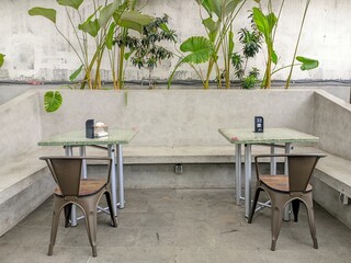 Minimalist caf&eacute; interior with concrete walls, green plants, and metal chairs creating a cozy and modern atmosphere