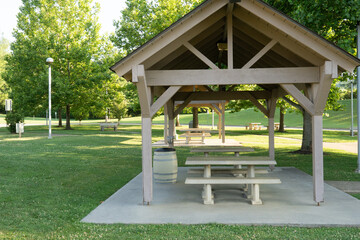 Wooden picnic table and bench covered by a small pavillion with trash can on a concrete pad along a highway rest area for travelers to take a break and have a meal