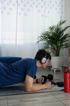 Man performing a plank exercise in his living room while listening to music with headphones, focused and concentrated. Concept of home workout, wellness, and active lifestyle