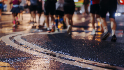 Night marathon runners crowd in the rain, sportsmen participants start running the half-marathon in the city streets with night lighting and illumination, group crowd of sportswomen joggers in motion