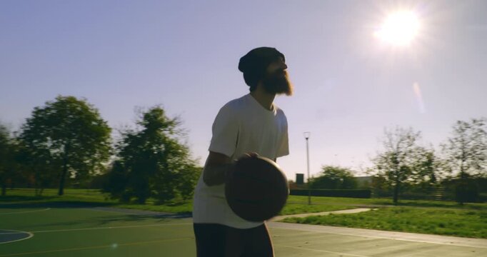 Slow motion of young man playing practice basketball on outdoor court at sunset at 1000 fps. Natural light, urban sport lifestyle and freedom concept.