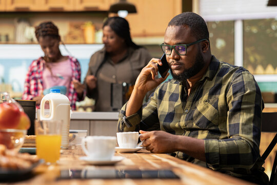 African american dad on a phone call for work during breakfast meal at home, interrupting family bonding time and morning routine to answer important calls. Father neglecting his children.