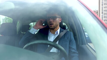 Disappointed young businessman talking on smartphone while sitting in the car and fastened with a seat belt. Transport, business, technology and people concept. Slow motion