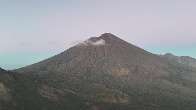 Majestic Volcanic Mountain Peak with Lush Green Slopes and Wispy Clouds Against a Clear Sky, Showcasing Nature's Grandeur and Serene Landscape