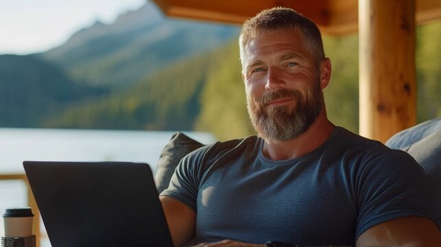 A man with a beard smiles while working on his laptop outdoors. He is surrounded by nature and mountains, embodying a relaxed and modern lifestyle. This image captures remote work and tranquility. AI