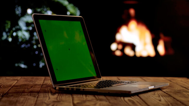 Laptop with a green screen chroma key screen against a glowing fireplace and Christmas tree. A warm, festive atmosphere for digital or themed layouts. - Powered by Adobe