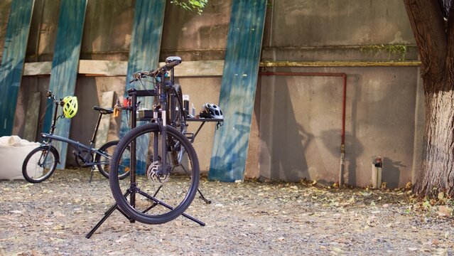 Contemporary bicycle awaits thorough examination and repair with professional equipment in yard as a summer activity. Damaged bike positioned on repair platform for fine-tuning and adjustment.