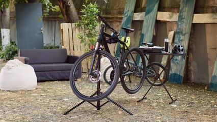 Shot of a broken bicycle on workstand with specialty tools for adjustment and repair in the background. Damaged bikes are seen in backyard awaiting fixing and correcting.