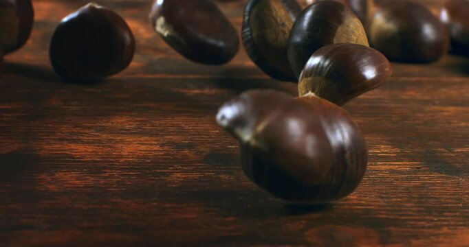 Slow Motion Close-up of shiny brown autumn chestnuts rolling on a wooden surface in cinematic motion at 1000 fps.