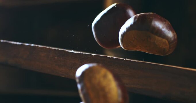 Slow motion macro of autumn chestnuts falling on rustic wood surface. Cozy, seasonal and organic atmosphere at 1000 fps.