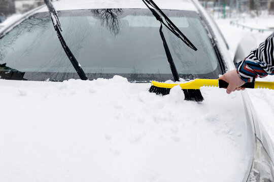 Man brushing snow ice from car windscreen,hood with brush.cleaning fresh snow layer after snowstorm on window.vehicle in extreme weather conditions in winter - Powered by Adobe