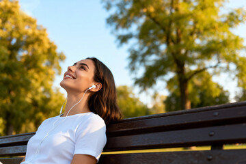 A woman enjoying music while sitting on a park bench in a sunny day