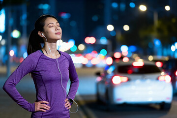 Young woman jogging in urban night with earphones on