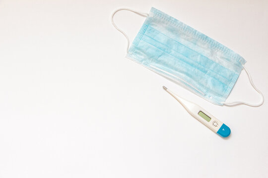 Medical face mask and digital thermometer placed on a clean white surface, symbolizing health awareness and safety measures during illness prevention and care