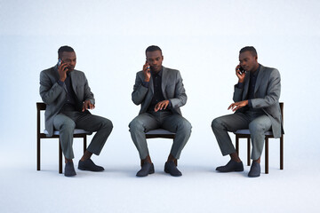 Three identical men in suits sitting on chairs using phones.