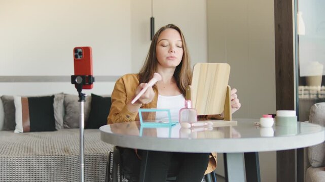 Blogger woman in a wheelchair applies makeup and smiles, making beauty vlog in a modern bedroom setting, showcasing independence and accessibility