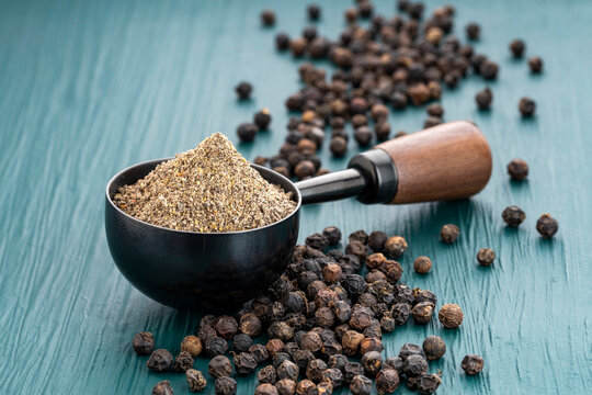 Piper nigrum - Ground black pepper in a spoon surrounded by whole peppercorns
