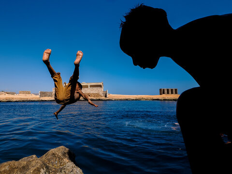 Silhouette of boy watching another mid-air dive into the sea near ruins on Socotra Island, Yemen