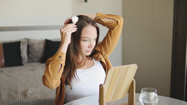A disabled woman puts cat ears on her hair in front of a mirror while sitting in a wheelchair, demonstrating her happiness and self-sufficiency.