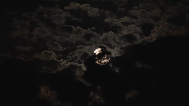 A bright full moon in a dark sky on a cloudy night with black clouds flying across the sky, like in thrillers and horror films. Shooting through a telephoto lens