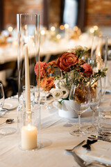 Elegant wedding table setup with soft candlelight, floral centerpiece of roses and chrysanthemums, and crystal glassware. Romantic fine dining atmosphere with warm bokeh lights in the background