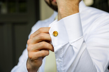 Close-up of a man adjusting his elegant white shirt cuff with a stylish golden cufflink. Concept of luxury fashion, men’s style, formal wear, and attention to detail