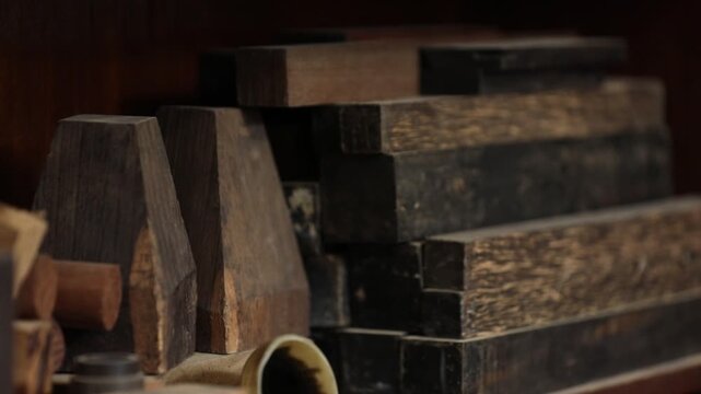 Vintage wooden letterpress blocks and tools stacked on a shelf in a workshop. Represents traditional printing, craftsmanship, typography, and history of media.