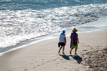Active senior Australian couple stroll on a beach along the Pacific ocean