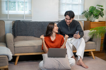 Happy asian couple celebrating success with laptop and phone