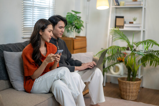 Asian couple relaxing on sofa using digital devices - Powered by Adobe