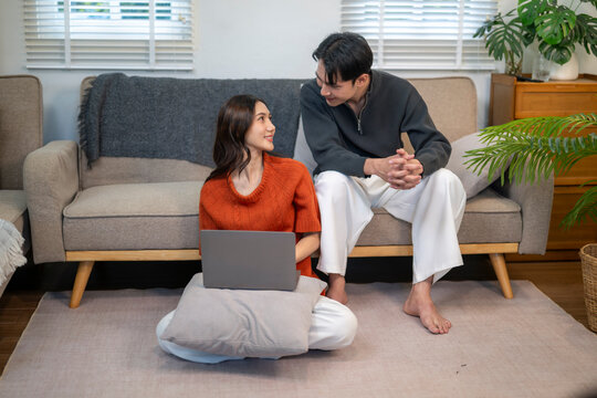 Asian couple relaxing at home talking and using laptop